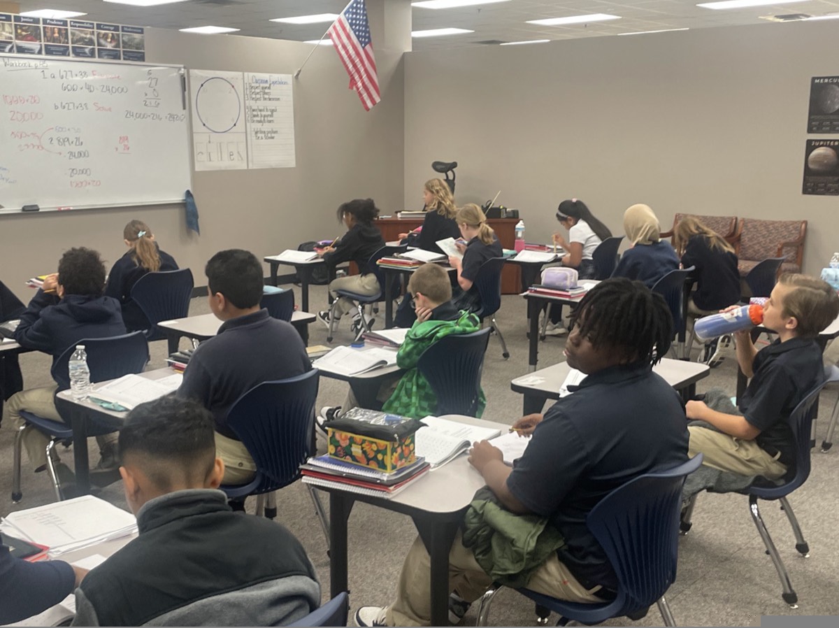 ACAR students in uniform at their desks during a lesson, with maths worked out on the whiteboard and the American flag at the front of the room