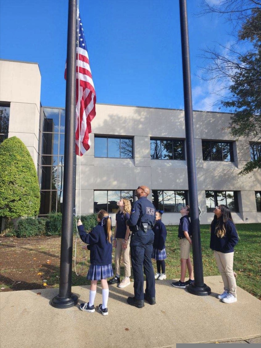 ACAR students in uniform raising the American flag outside the school with a school resource officer